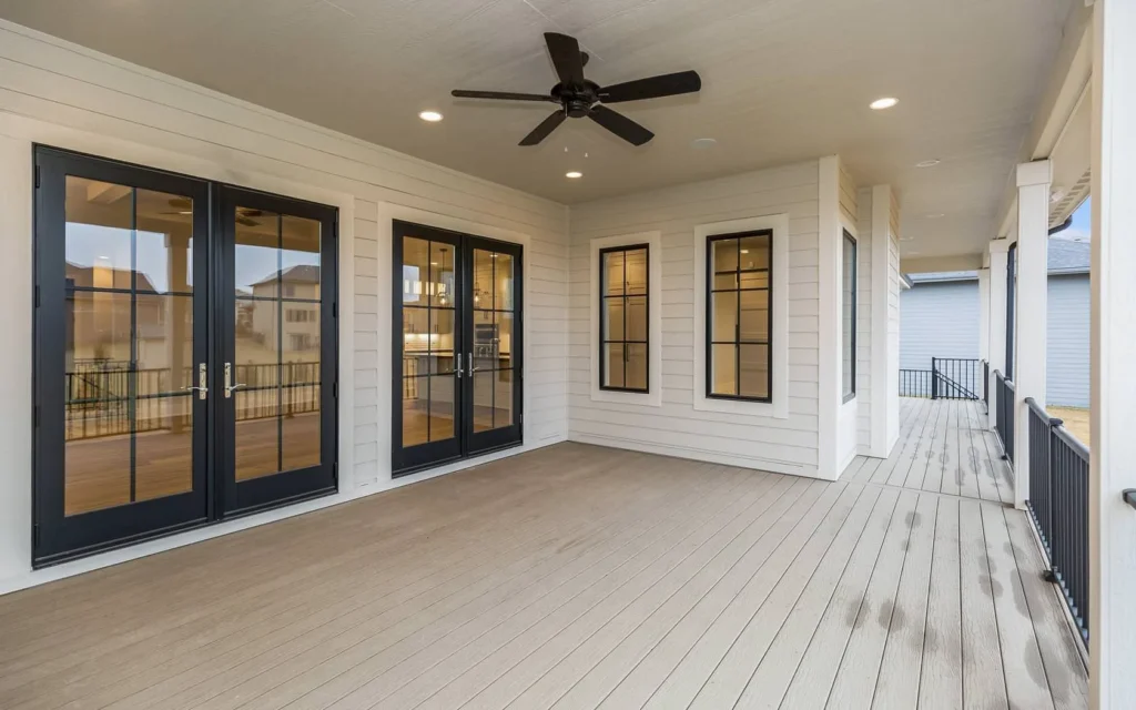 Spacious covered brown composite deck featuring black framed glass doors, ceiling fan, and recessed lighting.