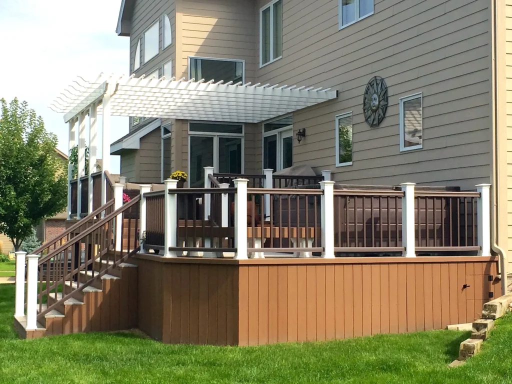 Elevated brown composite deck with white railing posts, access stairs, and an attached shade pergola.