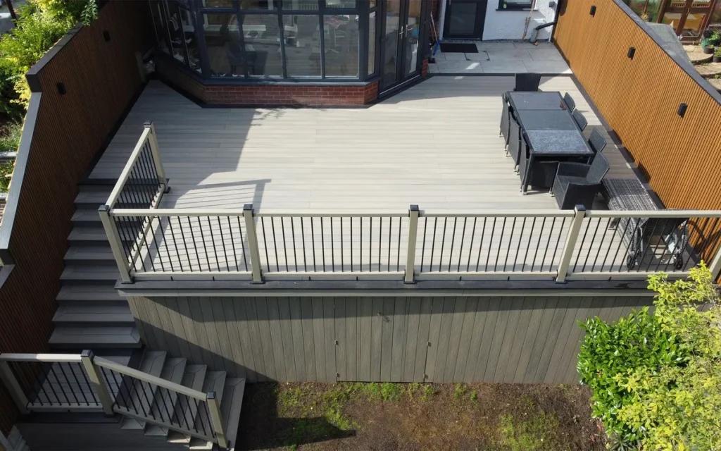High elevated beige composite deck with black metal railing, access stairs, outdoor dining area, and tall privacy fence.