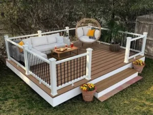 Small custom ground-level wood deck with white posts and black metal railing in a local backyard