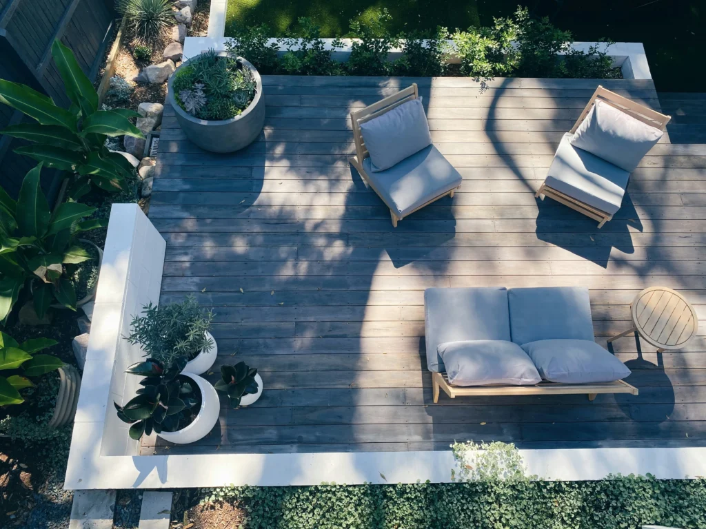 Top-down view of a modern grey composite deck patio featuring lounge furniture, potted plants, and white border walls.