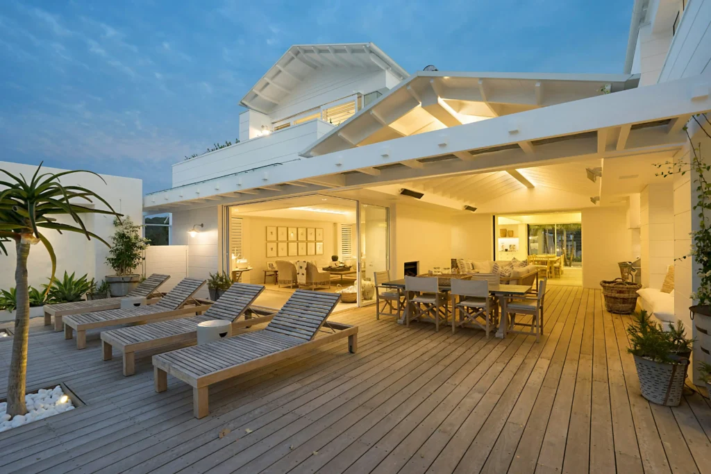 Luxury modern house with a spacious wooden pool deck, built-in ambient lighting, and timber lounge chairs.